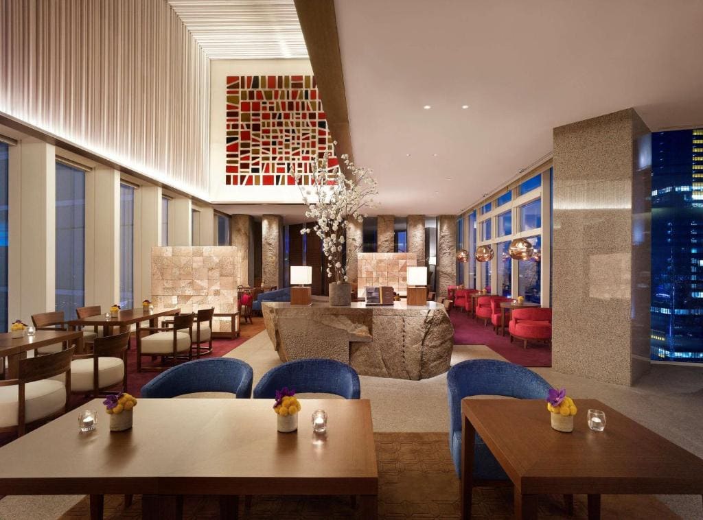 A modern, elegant restaurant with large windows, city views, stylish furniture, soft lighting, contemporary decor, and flower arrangements on wooden tables.