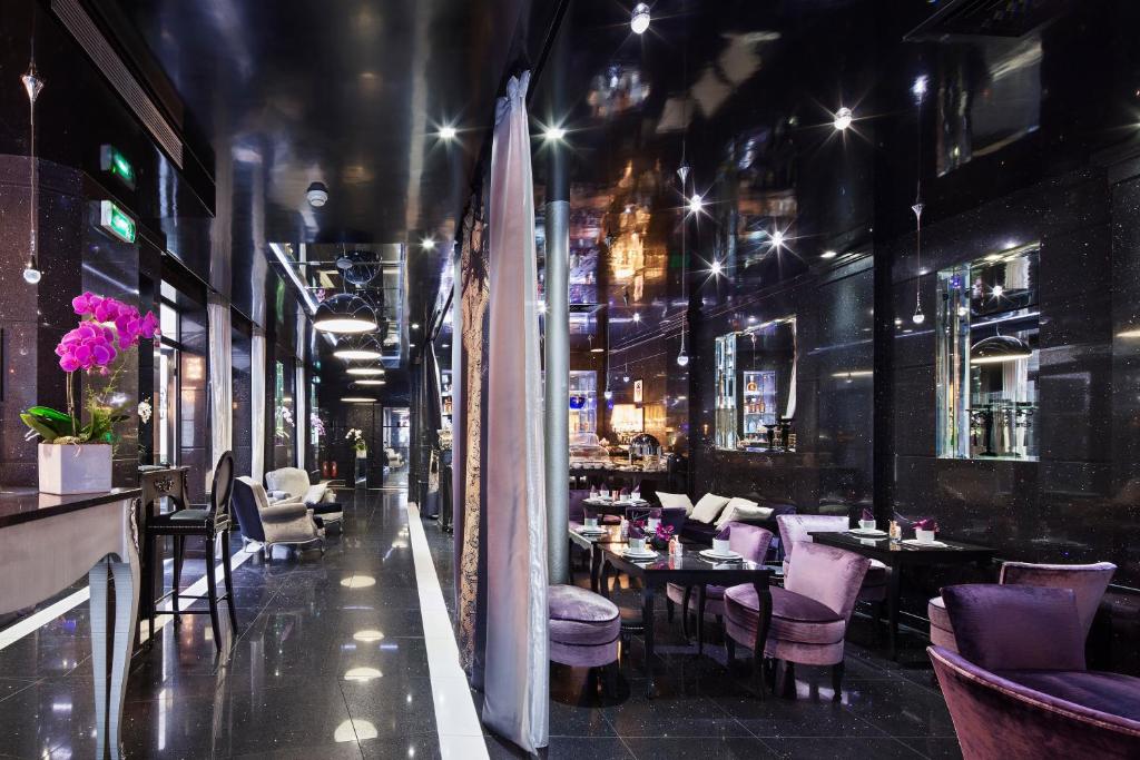 A modern, elegant lounge with glossy black floors and walls, purple and grey velvet chairs, small round tables, soft lighting, and decorative orchids, creating a luxurious, sophisticated atmosphere.