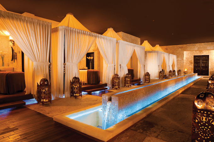 Luxurious spa room with glowing lanterns, private cabanas draped in white curtains, and a narrow water feature illuminated with soft blue lighting, creating a serene and elegant atmosphere.