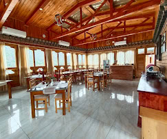 A cozy restaurant with wooden beams and large windows, letting in natural light. Tables are set with white napkins and cutlery, and the space has a warm, inviting atmosphere.