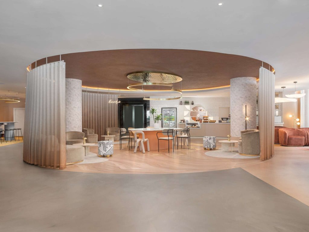 Modern lounge area with circular design, featuring curved sheer curtains, marble columns, contemporary seating, round tables, and soft lighting in a spacious, stylish interior.