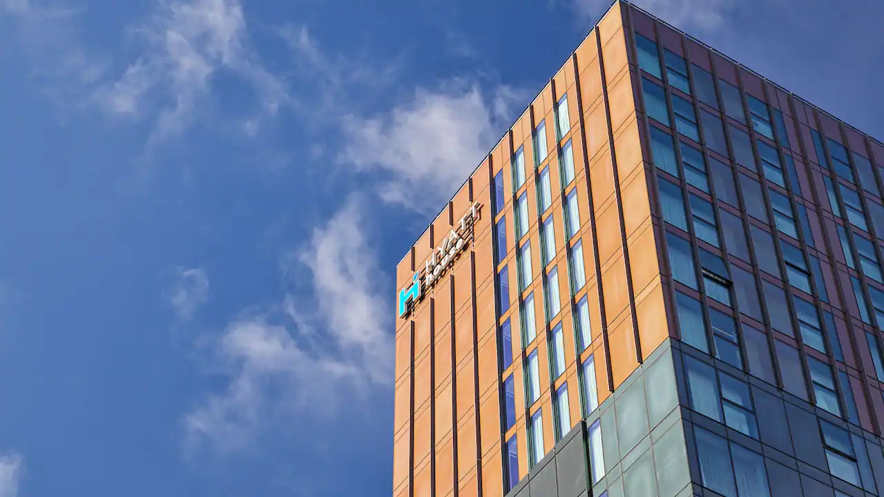 A modern high-rise building with an orange and glass exterior stands against a blue sky with scattered clouds. The TransUnion logo is visible near the top corner of the building.
