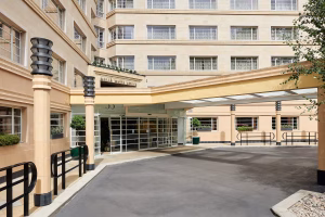 The image shows the entrance to a modern, multi-story building with large windows, a covered driveway, and decorative pillars. The entrance has a sign reading MEDIA WORKS BUILDING above glass doors.