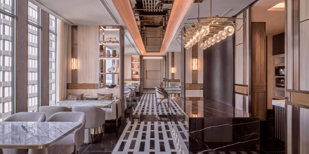 Modern, elegant restaurant interior with marble tables, plush seating, large windows, contemporary lighting, geometric flooring, and neutral colors, creating a bright and sophisticated dining atmosphere.