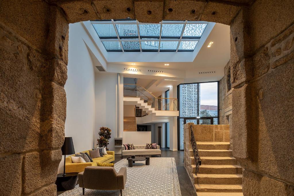 Modern living room with high ceilings, a glass skylight, stone archway entrance, floating staircase, and contemporary furniture, blending historic stonework with sleek, minimalist decor.