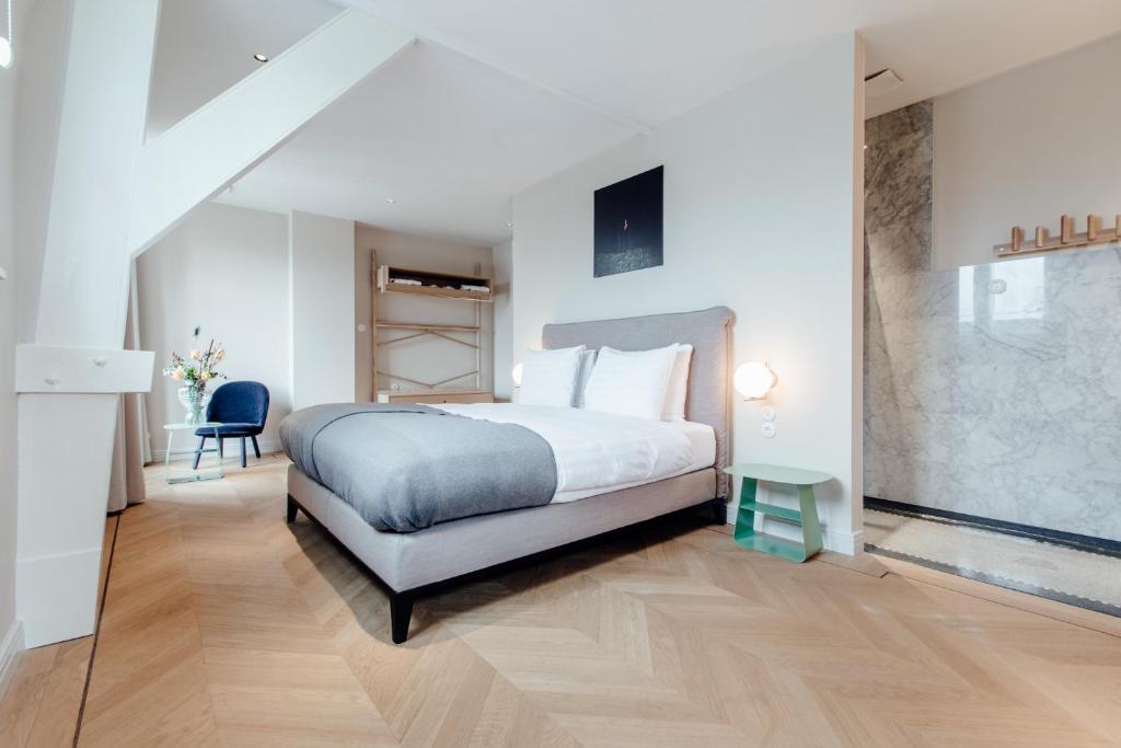 Modern bedroom with a double bed, white bedding, a gray throw, bunk beds in the background, a blue chair, a green bedside table, wooden floors, and a marble accent wall by a walk-in shower.
