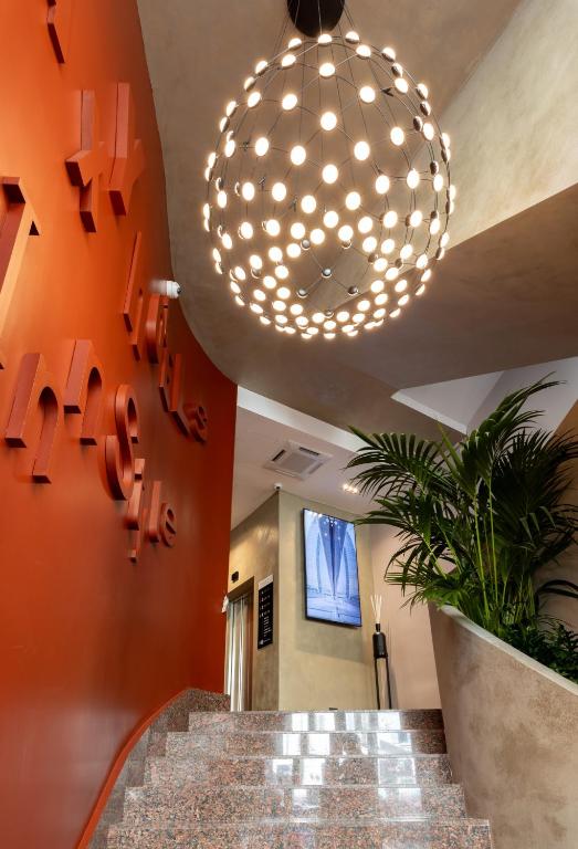 A modern stairway with polished stone steps, red accent wall with raised letters, large spherical pendant light, indoor plants, and contemporary decor including framed art and a reed diffuser.