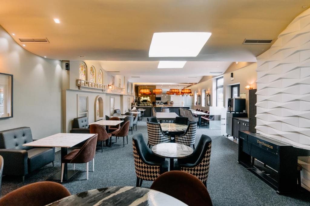 Modern restaurant interior with marble tables, cushioned chairs, and booths. Soft lighting, wall art, and decorative arches create a cozy, upscale atmosphere. The space feels open and inviting, with a neutral color scheme.