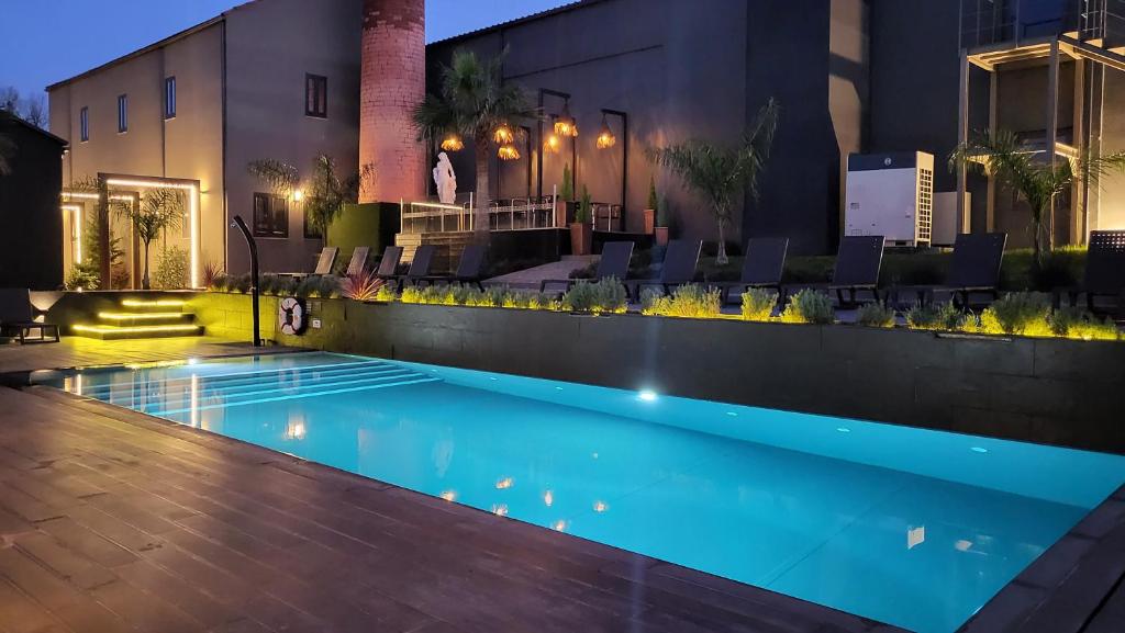 A modern outdoor swimming pool at dusk, surrounded by lounge chairs, palm trees, soft accent lighting, and contemporary buildings with large windows.