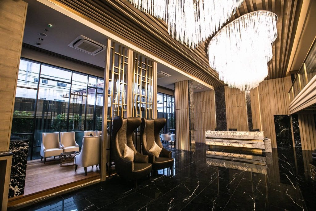 A modern hotel lobby with black marble floors, tall chandeliers, sleek high-back chairs, a marble reception desk, and large floor-to-ceiling windows letting in natural light.