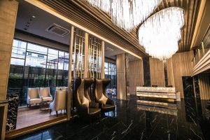 A modern hotel lobby with black marble floors, tall chandeliers, sleek high-back chairs, a marble reception desk, and large floor-to-ceiling windows letting in natural light.