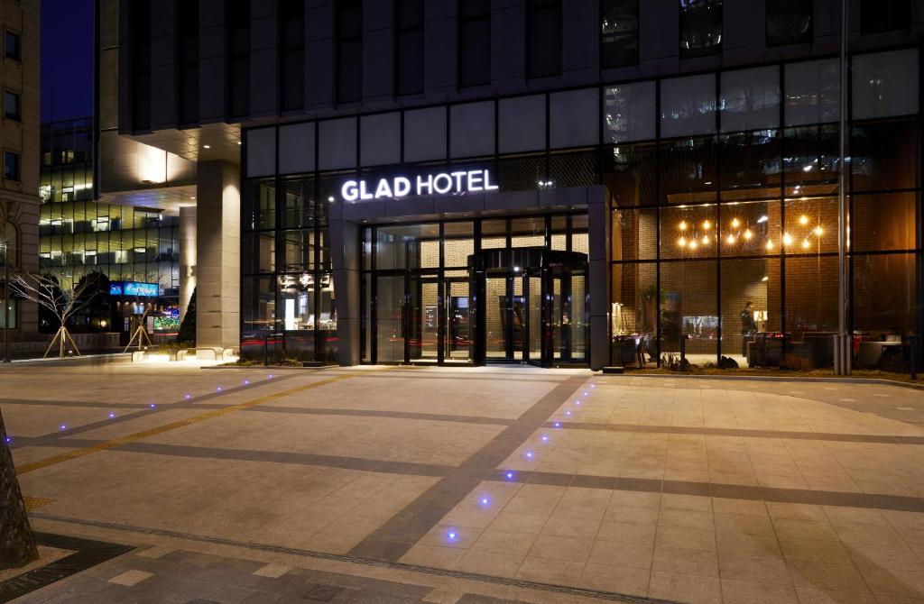 The entrance of GLAD Hotel at night, with illuminated signage, glass doors, warm interior lights, and blue pathway lights on the paved area in front.