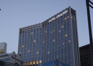 A tall, modern building with many windows and a sign reading HOTEL GRACERY near the top, photographed at dusk against a clear sky.