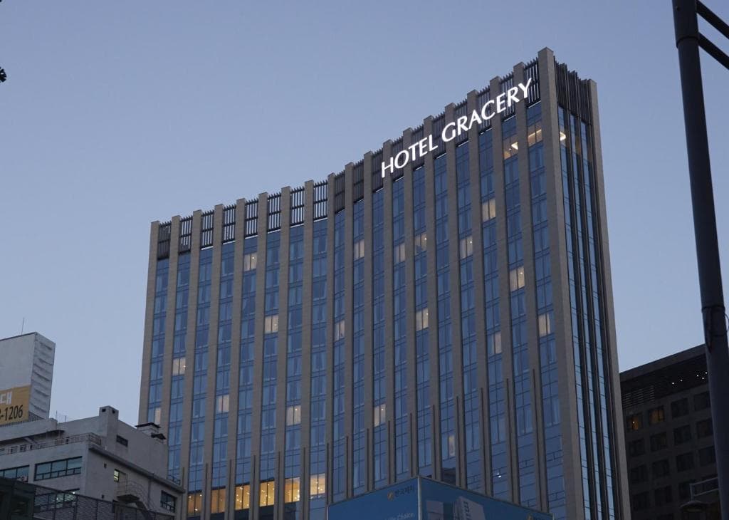 A tall, modern building with many windows and a sign reading HOTEL GRACERY near the top, photographed at dusk against a clear sky.