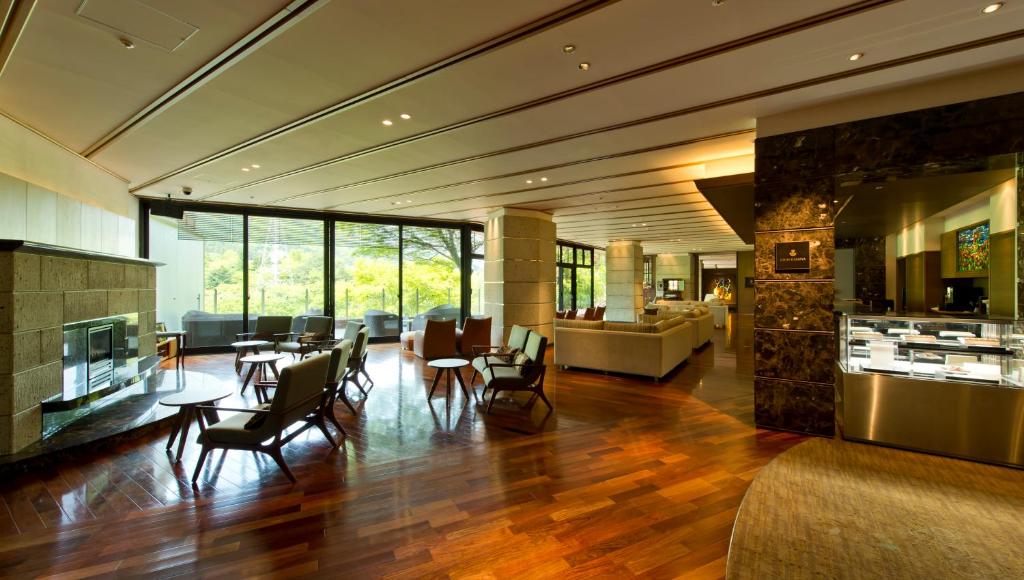 Spacious, modern lounge with wooden floors, contemporary chairs and sofas, a fireplace, large windows offering a view of greenery, and bright natural light filling the room.