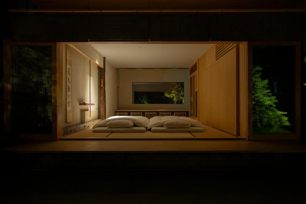 A traditional Japanese room with tatami mats, two futons with pillows, wooden sliding doors, soft lighting, and a view of a garden outside at night.