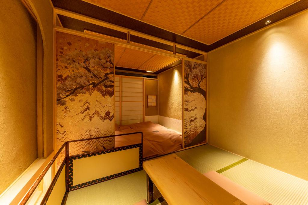 A traditional Japanese room with tatami mats, sliding shoji screens, and floral-patterned partition panels. A low wooden bench sits in the foreground, and a futon bed is visible behind the partition. Soft, warm lighting fills the space.
