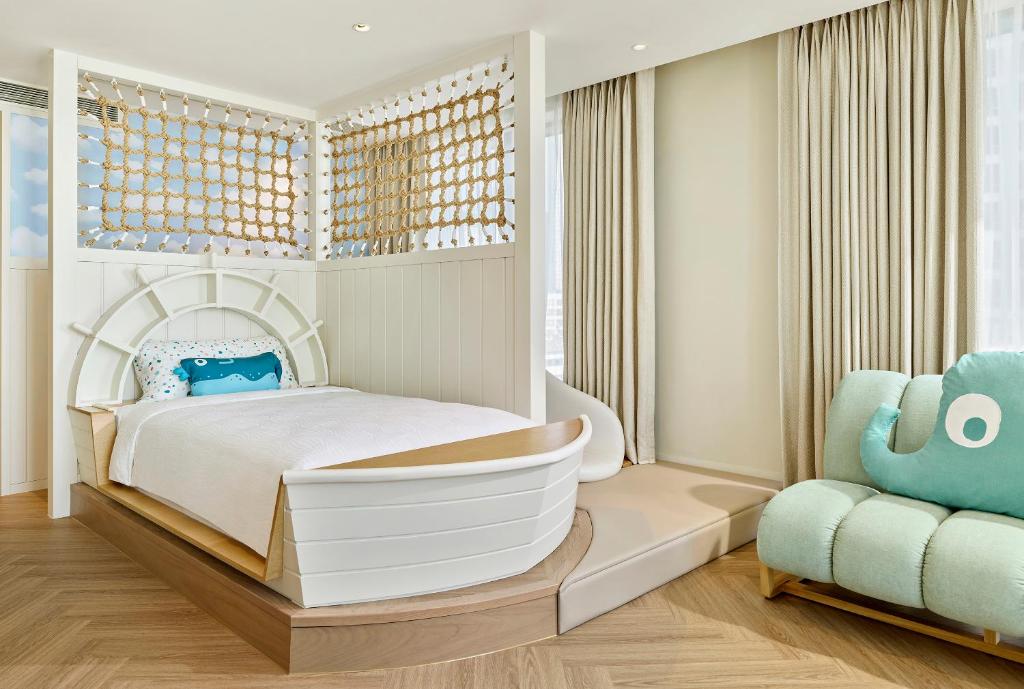 A cozy, nautical-themed children’s bedroom with a boat-shaped bed, ocean-themed pillow, rope net decor, beige curtains, wood floor, and a light blue elephant-shaped sofa. Natural light fills the bright room.