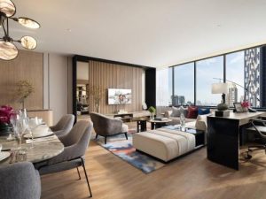 Modern living and dining area with large windows, city views, contemporary furniture, a TV mounted on a wood-paneled wall, a dining table set for six, and a work desk by the window.