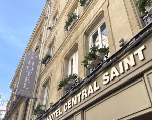 Hotel Central Saint Germain building facade with beige stone exterior, multiple windows with flower boxes, and a vertical sign reading HOTEL Central St Germain in French, seen from a street-level upward angle.