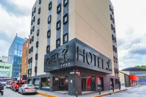 A modern multi-story building with black and beige exterior, featuring large signs that read HOTEL FLAMENCOS and a flamingo logo. Several cars are parked along the street in front.