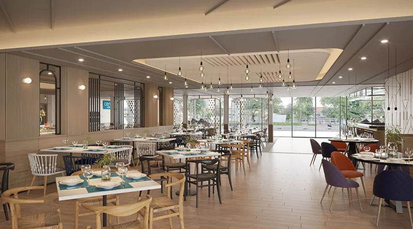 Modern restaurant interior with wooden floors, neatly set tables, a mix of chairs, pendant lighting, and large windows providing a bright view of greenery outside. The atmosphere is open and inviting.