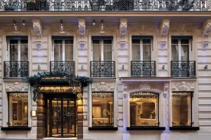 Elegant facade of a luxury hotel with ornate balconies, large windows, and decorative stonework. Warm lights illuminate the entrance and lower windows, and wrought iron details accent the building’s classic architecture.