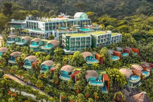Aerial view of a modern, multi-level resort nestled in lush greenery, featuring dome-shaped villas with private pools, large terraces, and rooftop amenities, surrounded by dense tropical forest.