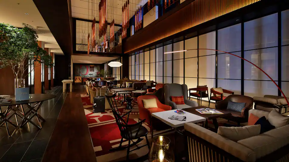 A modern hotel lounge with stylish seating, warm lighting, contemporary decor, large windows, and patterned rugs, creating a cozy and inviting atmosphere.
