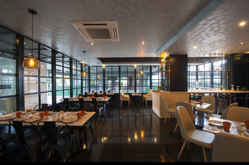 Modern restaurant interior with dark glossy floors, glass walls, and ceiling lights. Tables are set for dining, with black and white chairs neatly arranged in a clean, spacious, and contemporary setting.
