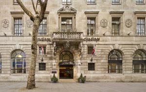 The image shows the exterior of a grand stone building with arched windows, British flags, and a central entrance to Citadines. A leafless tree stands on the sidewalk in front.
