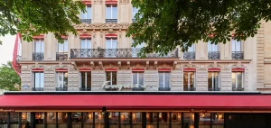 A historic building with ornate balconies and red awnings, featuring the name Fouquet’s above the entrance. Green tree branches frame the upper part of the image.
