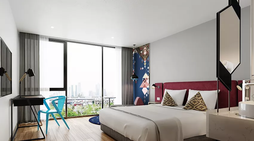 Modern hotel room with large window, city view, double bed with patterned pillows, wall art, desk with lamp, blue chair, mounted TV, and wood flooring. Room decor is contemporary with geometric accents.