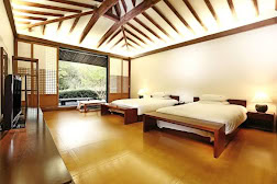 Spacious room with two double beds, wooden floors, exposed beam ceiling, large window with a view of greenery, and minimalistic Japanese-inspired decor.