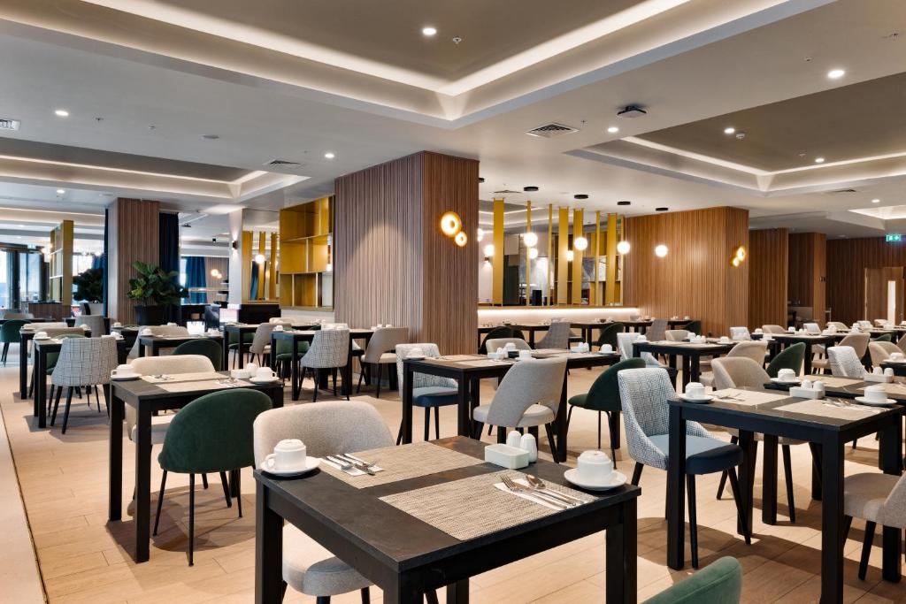 A modern, spacious restaurant dining area with neatly arranged tables and chairs, warm wooden accents, soft lighting, and place settings prepared for guests. The atmosphere is clean and inviting.