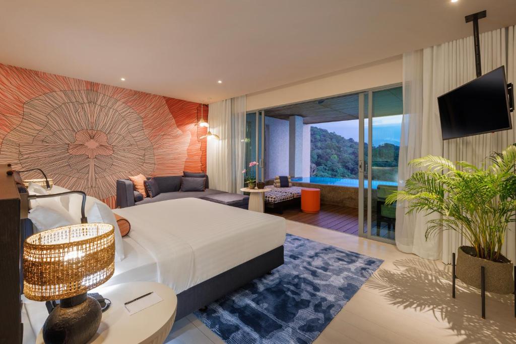 A modern hotel room with a large bed, artistic wall mural, cozy seating area, TV, and sliding glass doors opening to a balcony with outdoor seating and a scenic view of hills and water.