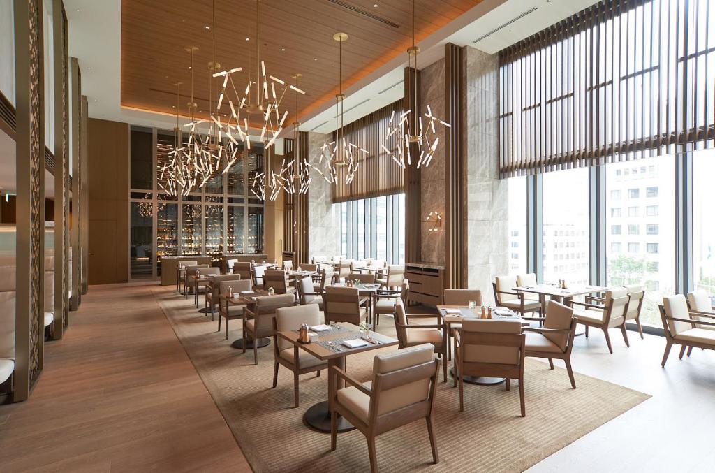 A modern, spacious restaurant with tall windows, elegant lighting fixtures, and neatly arranged tables and chairs on wooden floors. Natural light fills the room, creating a bright and inviting atmosphere.