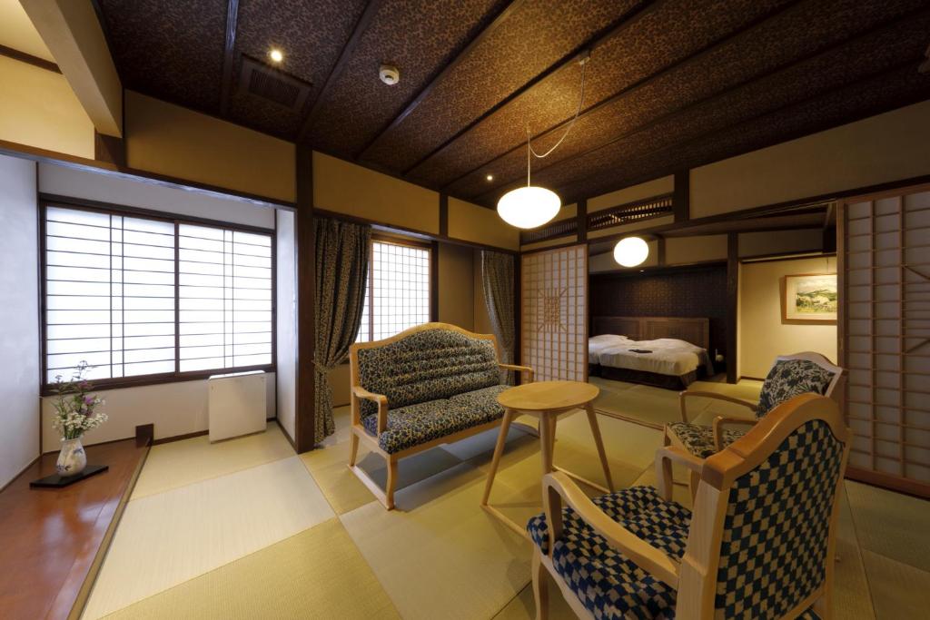 A traditional Japanese-style room with tatami mats, a low wooden table, three patterned chairs, shoji screen doors, and a bedroom area with twin beds in the background. Soft lighting creates a calm atmosphere.