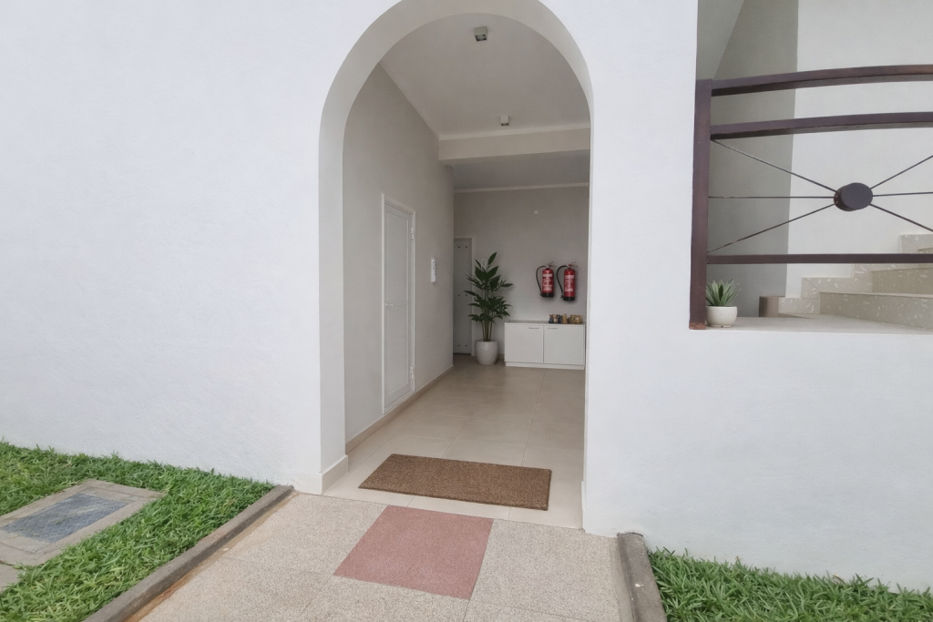 Building entrance through arched doorway. Threshold is flush between
exterior paved approach and interior tiled floor. No steps on the main entrance route. Entrance mat just inside doorway. Steps visible to right leading to an upper level but not on the primary entrance path. Interior lobby has smooth tile flooring.