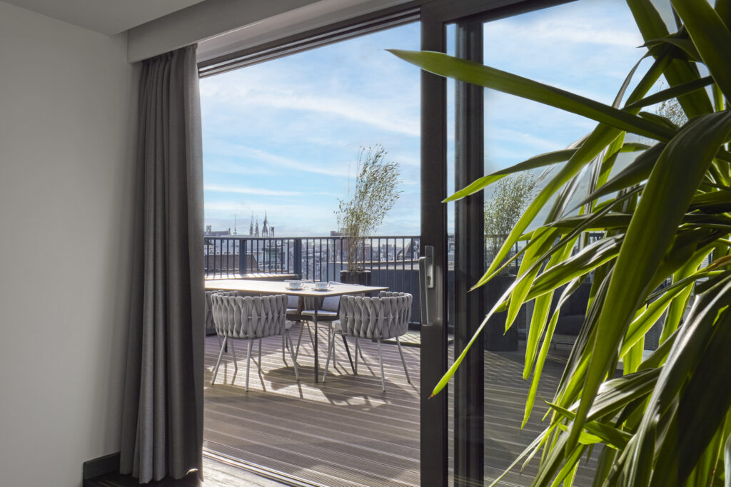 View from Penthouse de Witt through sliding doors to the private terrace with dining setting overlooking the Amsterdam skyline.