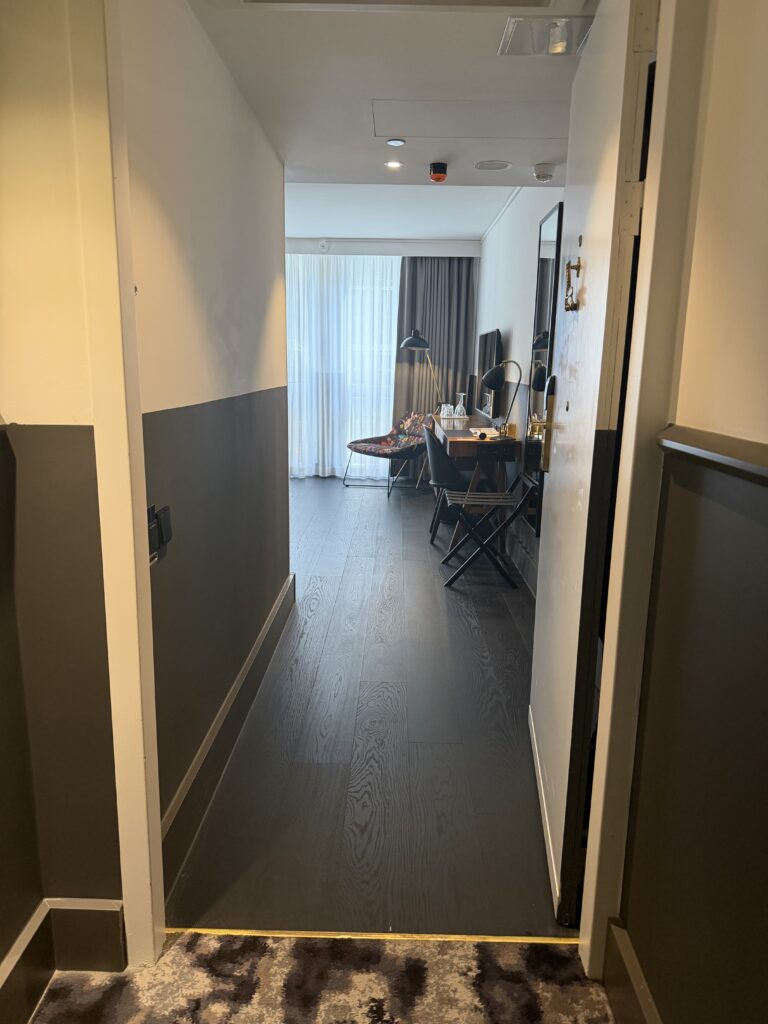 View from accessible bedroom doorway into room interior with desk and window beyond, wood flooring throughout.