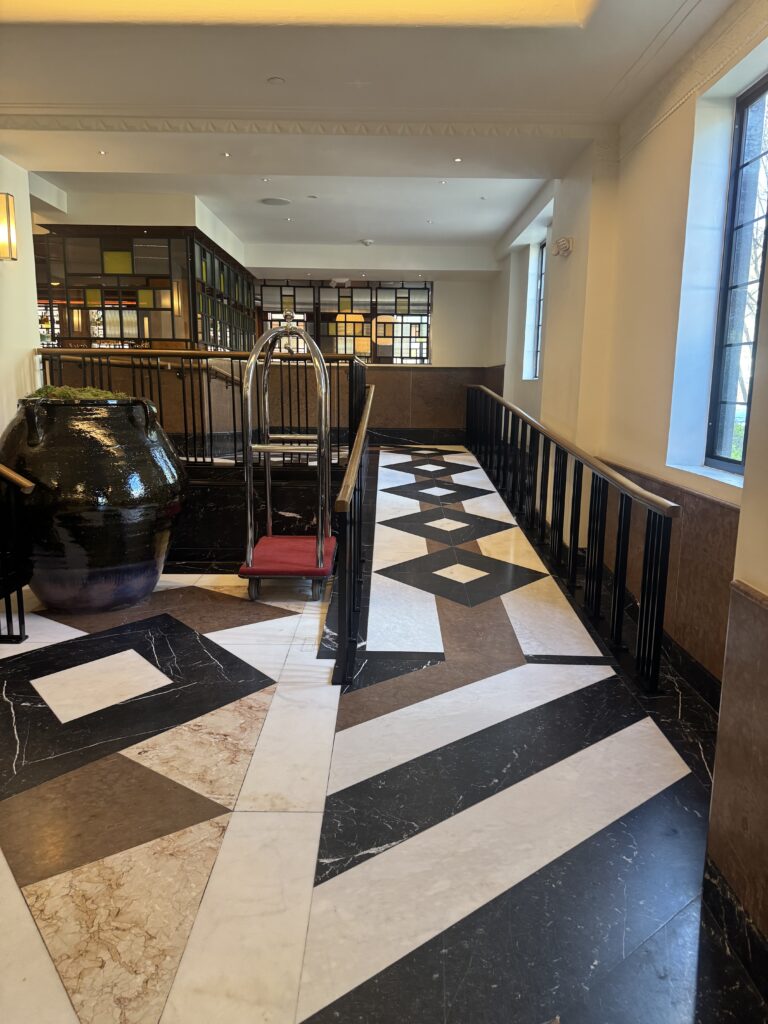 Internal lobby ramp at Lyle Washington DC. A handrailed ramp runs alongside the steps between lobby levels. The floor is marble inlay in dark and pale tones with deeper accent stones. Black metal handrails with oak tops run along both sides of the ramp.