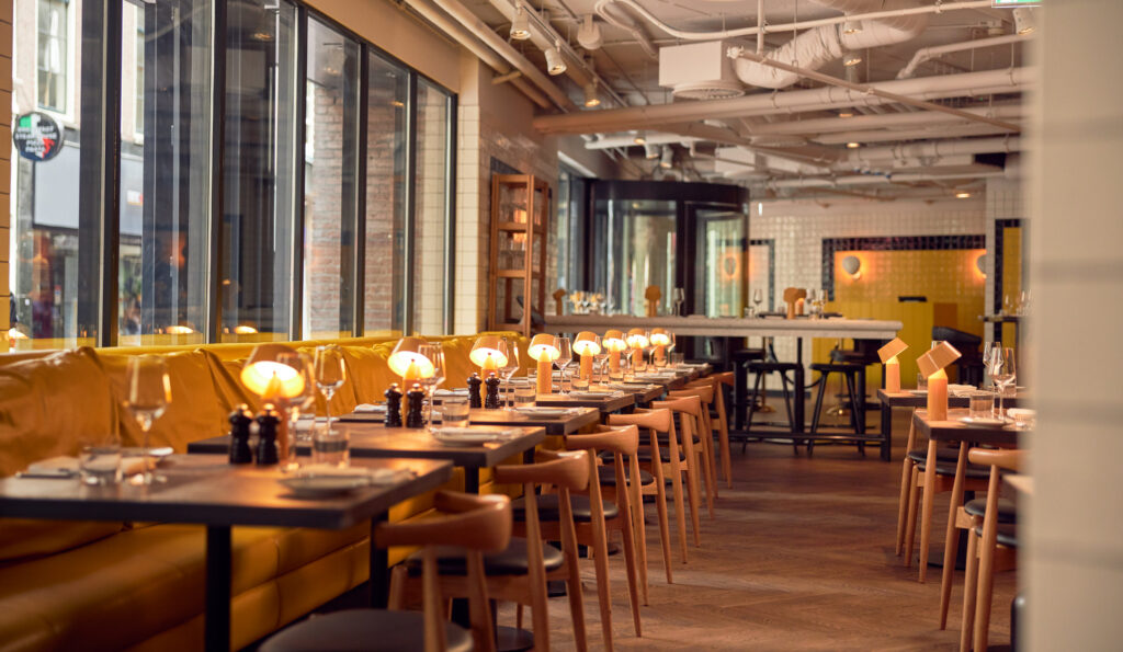 Celia restaurant at Kimpton de Witt with yellow leather banquette running along the window and individual table lamps at each setting, herringbone wood floor with high-top bar seating at the rear.