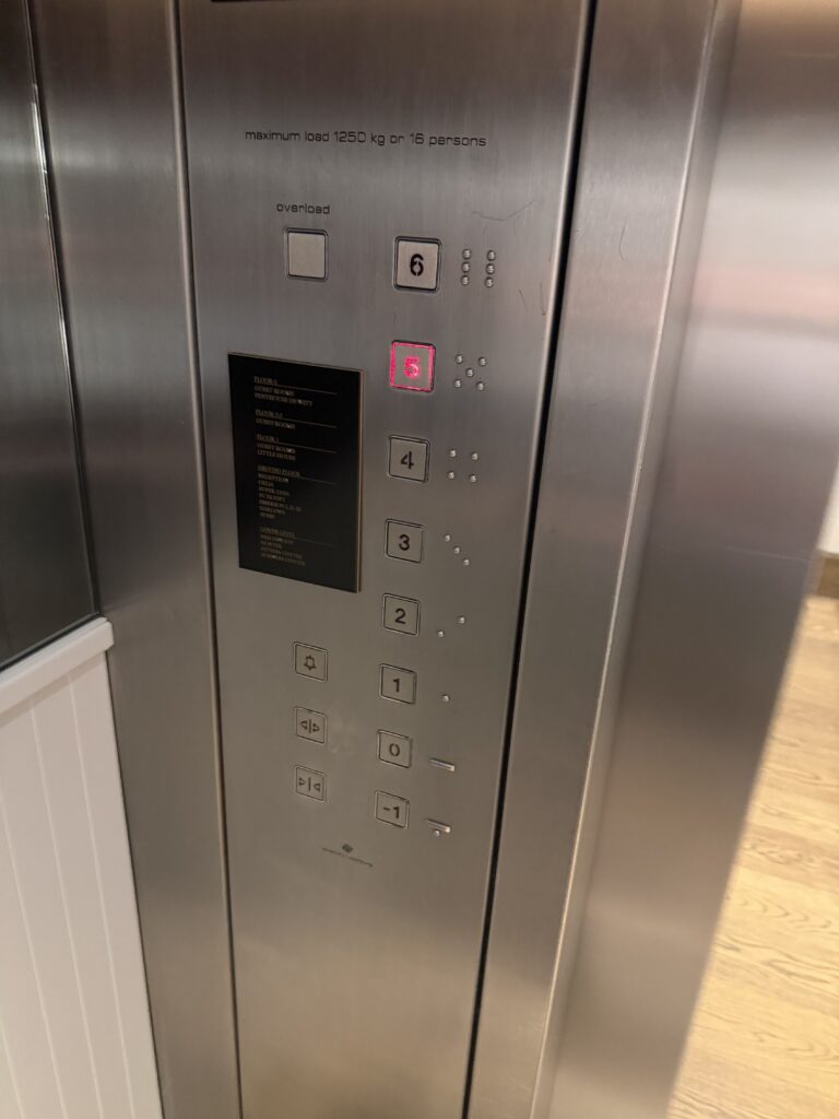 Lift control panel with braille-marked floor buttons and printed floor index plate.