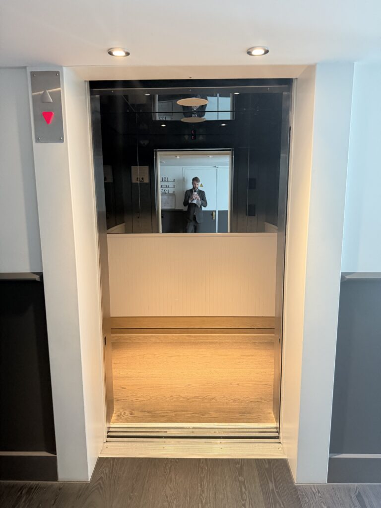 Lift cab viewed through open doors showing mirror at rear and floor space.