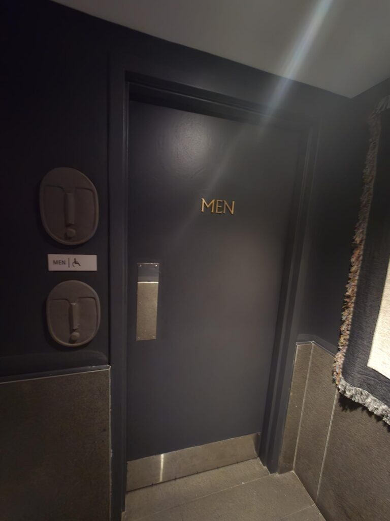 Entrance to the accessible public washroom at Hotel Park Ave NYC. Door marked “Men” with a wheelchair-access symbol on the adjacent wall plate, level threshold.