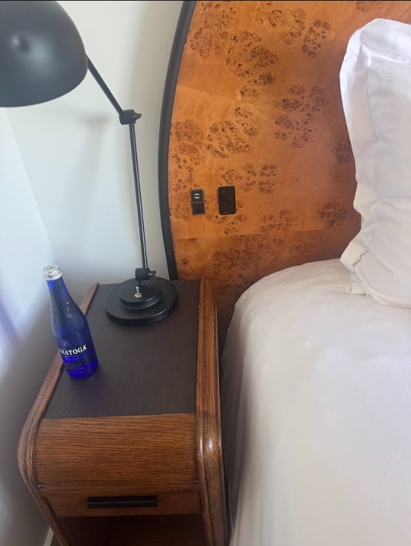 Bedside controls in a guest room at Lyle Washington DC. Burl headboard with an inset socket and rocker switch panel within reach of the bed. Bedside table with reading lamp.
