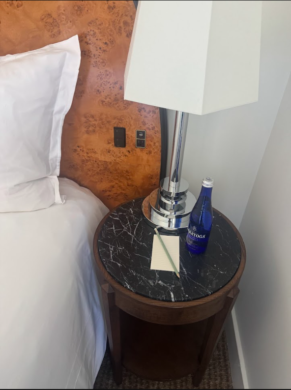 Bedside controls in a guest room at Lyle Washington DC. Burl headboard with an inset socket and rocker switch panel within reach of the bed. Bedside table with reading lamp.